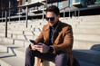© baranq - Closeup of happy man texting message while sitting on stairs during sunny spring or autumn day in the city