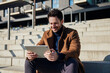 © baranq - Closeup of smiling man wearing coat relaxing with digital tablet on stairs in city