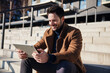 © baranq - Closeup of smiling man wearing coat sitting with digital tablet on stairs in city