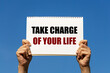 © Tepsarit - Take charge of your life text on notebook paper held by 2 hands with isolated blue sky background. This message can be used as business concept about taking ownership of your life.