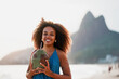 © oscargutzo - headshot portrait young black brazilian woman posing and smiling holding coconut water on the shore of the beach in Ipanema Brazil