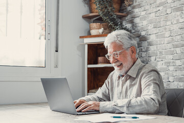 Wall Mural - Aged remote worker. Concentrated senior male in glasses work on laptop from home office read email electronic document. Old age man employee freelancer sit at kitchen table by pc typing report online.