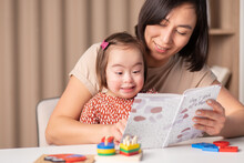 Cute Child With Down Syndrome Girl With Mom And Book At Home