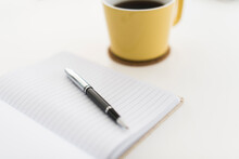 Close-up Of Book And Pen By Coffee Cup On White Background