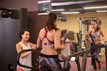 Smiling Woman Looking At Friend Running On Treadmill By Mirror In Gym