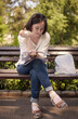 © Cavan Images - Full length of young woman reading paper while sitting on bench at park