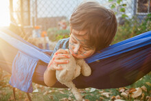 Close-up Of Boy With Paint On Face Kissing Teddy Bear While Relaxing In Hammock At Yard