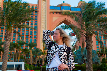 Wall Mural - The image depicts a stunning blonde visitor taking advantage of Dubai's hospitality. Her hair is blowing in the breeze, giving her a fun aspect, and she has a warm, welcome grin.
