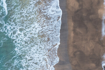 Wall Mural - View of a beach from a drone. Turquoise water with waves on one side and snow-covered sand on the other.