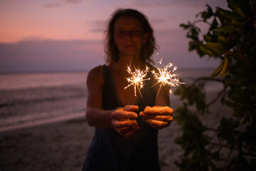 Sticker - woman holding sparkles celebrating on tropical beach