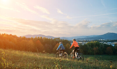 Mother and son ride a bike. Happy cute boy in helmet learn to riding a bike in park on green meadow in autumn day at sunset time. Family weekend.