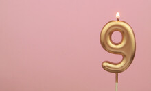 Burning Gold Birthday Candle On Pink Background, Number 9. Large Copy Space For Text.