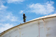 © chitsanupong - Male worker down height tank roof rope access safety inspection thickness weld of storage tank.