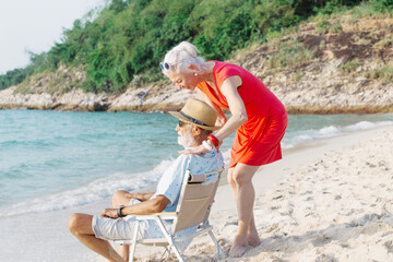 Wall Mural - Beautiful and happy senior couple in love sitting on the beach at sunset and enjoying amazing sea view at tropical sunset together