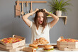 © sementsova321 - Portrait of crazy irritated shocked woman wearing white T-shirt sitting at table in kitchen, pulling her hair, a girl on a diet, surrounded by delicious junk food, does not know how not to break loose