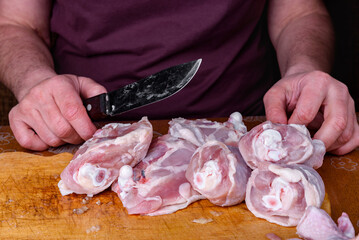 Wall Mural - Female hands carves raw chicken legs on wooden board in kitchen.