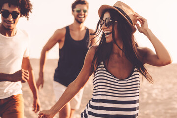 Wall Mural - Group of beautiful young people running along the beach and smiling