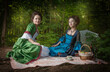 Two young beautiful women in long medieval dresses having picnic