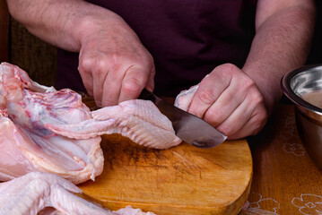 Wall Mural - Female hands cutting raw chicken wings on wooden board in kitchen.