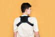 A young guy has a stooped back and bad posture, so he often wears a special bandage to support the back muscles, align the posture, medical concept