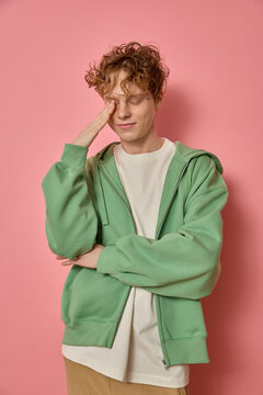 Calm relaxed young handsome smiling man 20s wearing colourful clothes touching his face with his hand and feeling a bit tired of working isolated on pink background. Teenager feeling confused and shy.