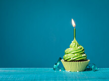 Green Cupcake With Lit Candle On A Blue Background.