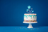 Fototapeta Tęcza - White birthday drip cake with teal ganache, star toppers and fun candles over dark blue background