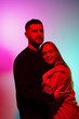 © arthurhidden - Young bearded man hugging girlfriend gently while standing in studio with colourful neon illumination