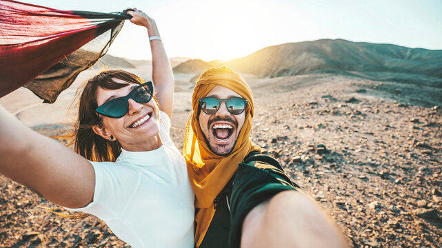 happy couple of travelers taking selfie picture in rocky desert - young man and woman having fun on 