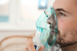 Sick man using inhalation nebulizer indoors, closeup. Space for text