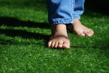 The Feet Of A Woman Wearing Jeans Step On The Grass