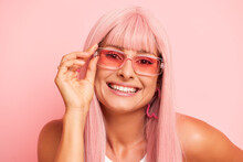 Long Hair Blond Woman In Pink Sunglasses With Bright Smile And Manicured Nails Holds The Glasses Frame And Smiles Positively Isolated Next To The Pink Wall. Eyewear Concept