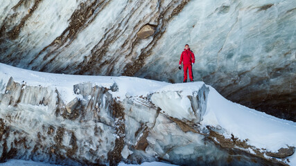 Wall Mural - The guy in red is standing on top of the glacier. Frozen moraine lake in the mountains. Lots of snow. Aerial view from a drone of people, mountains and trails in the snow. The ice is breaking down