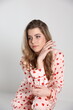 © Anhelina  - beautiful blonde girl sits on a chair on a white background in pajamas. pajamas with hearts. Valentine's Day. studio photo shoot in satin pajamas with a heart print. clothes for sleep and home