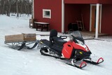 Fototapeta  - A snowmobile with wooden trailer  stands by wooden Scandinavian red house.
