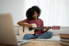 Focused African Girl Playing Acoustic Guitar And Watching Online Course On Laptop While Practicing At Home. Online Training, Online Classes.
