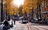 Fototapeta  - Amsterdam, Netherlands. Street view, Modern tram, public transport moving by Autumn evening sunny day. Bicycle on the road