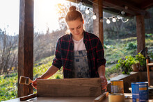 Woman Carpenter In A Plaid Shirt Varnishes Oiling A Wooden Board On The Terrace Of A Country House