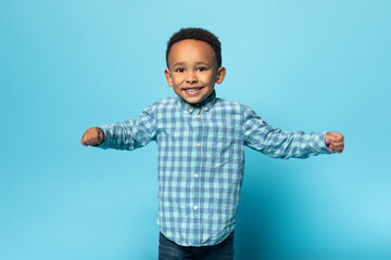 Wall Mural - Portrait of adorable african american boy in casual clothes smiling at camera, standing over studio wall, free space