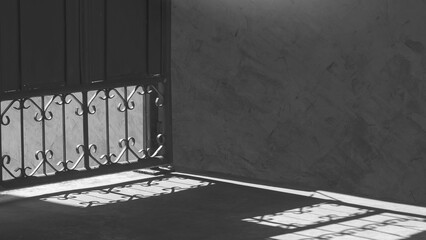 Wall Mural - Light and shadow of wrought iron pattern shines through the metal entrance door onto the corridor and loft concrete wall inside of house in black and white style