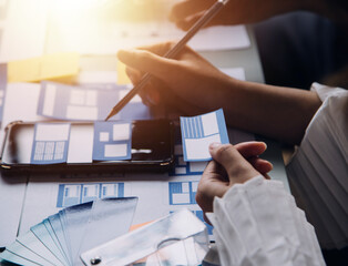 Close up ux developer and ui designer brainstorming about mobile app interface wireframe design on table with customer breif and color code at modern office.Creative digital development agency