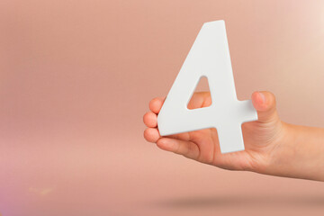 number four in hand. Hand holding white number 4 on red background with copy space. Concept with number four. Birthday 4 years, fourth grade, four day work week