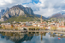 Sunny Aerial Cityscape Of Lecco Town On Spring Day. Picturesque Waterfront Of Lecco Town Located Between Famous Lake Como And Scenic Bergamo Alps Mountains.