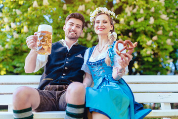 Wall Mural - Couple in Bavaria sitting on bench toasting with beer hugging each other