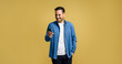 © Moon Safari - Smiling mid adult handsome man browsing social media on smart phone while posing with hand in pocket on isolated yellow background
