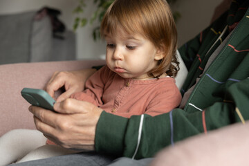 A little girl sits in her arms. an adult in a home chair and is surprised by what he sees on his phone