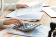 Female accountant working with calculator and documents at table in office, closeup