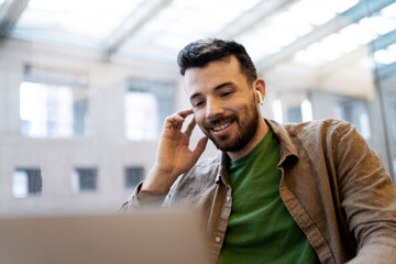 Attractive, smiling man in wireless earphones having video conference, using laptop. Successful businessman has online communication with partner. Concept of online education, remote work