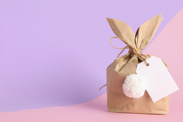 Wall Mural - Easter bunny gift bag with blank tag on lilac and pink background