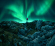 Northern lights and young woman on mountain peak at night. Aurora borealis, stones and silhouette of alone girl on mountain trail. Landscape with polar lights. Starry sky with bright aurora. Travel
